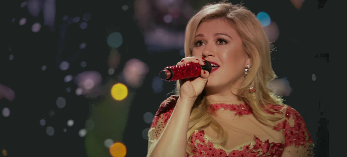 Kelly Clarkson mengenakan dress merah, sedang tampil di salah satu event.